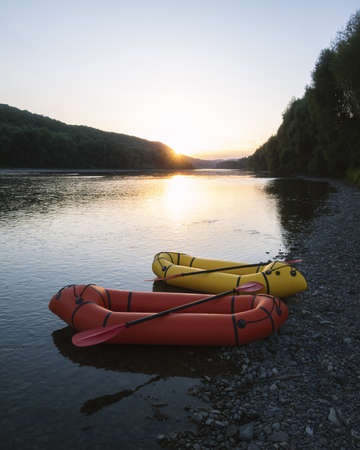 Orange and yellow packrafts rubber boats with padles on a sunrise river. Packrafting. Active...