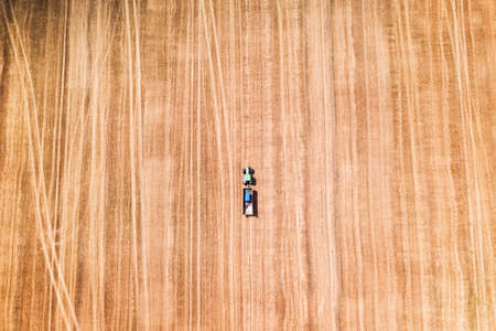 Lonely tractor in a wheat field during the harvest while waiting for the combine. Aerial top viewの写真素材