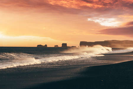 Incredible sunset view on stormy Atlantic ocean on Black Beach, Vik, Iceland. Big waves, orange sky and dark rocks. Landscape photographyの写真素材