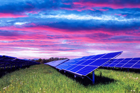 Solar panel on purple sunset sky background. Green grass and cloudy sky. Alternative energy concept