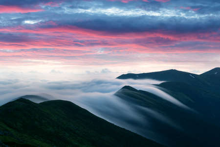 Amazing flowing morning fog in spring mountains blurred from long exposure. Beautiful sunrise on background. Landscape photographyの写真素材