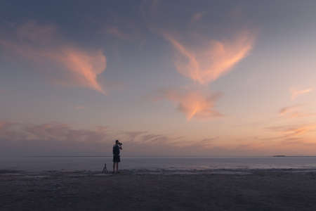Photographer taking photo with tripod of ocean sunrise. Sunset on the sea with red glowing cloudy...