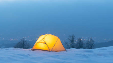 Yellow tent lighted from the inside against the backdrop of glowing city lights