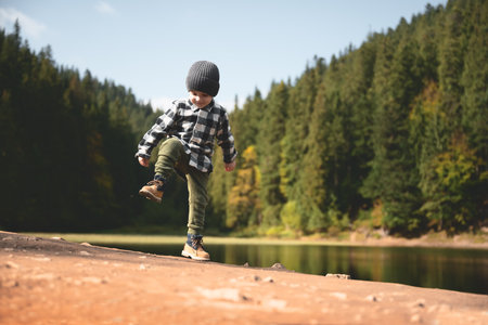 Small kid in a plaid shirt and gray hat on the forest lake coastの写真素材