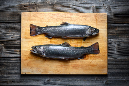 Two arctic char fish on wooden cutting board on rustic tableの写真素材