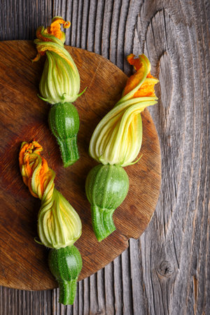 Three young zucchini with flowers on wooden cutting boardの写真素材