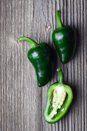 Three green mexican jalapeno hot peppers on rustic wooden table