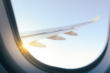 View of sun with beams in clear sky and wing from a plane windowの写真素材