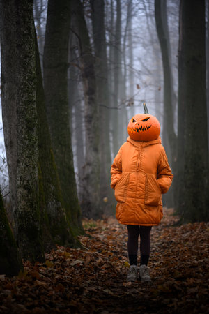 Girl in orange jacket wears spooky pumpkin headの写真素材