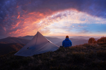 Tent and hiker set against breathtaking sunset sky in autumn mountainsの写真素材
