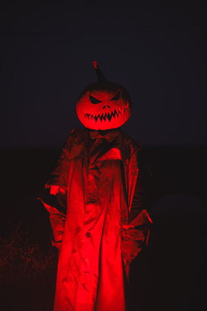 Creepy scarecrow in an old torn cloak with a carved pumpkin head