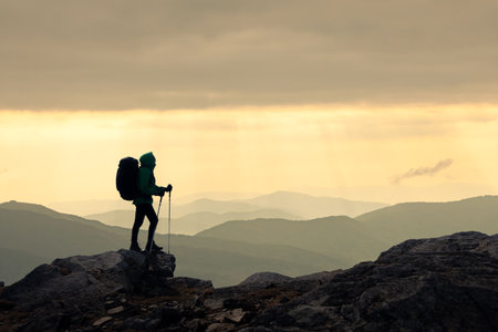 Backlit silhouette of a tourist with a backpack gazing at majestic sunset