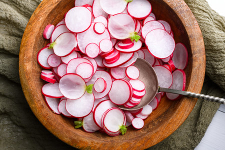 Close up of sliced radishes in wooden bowl with spoon