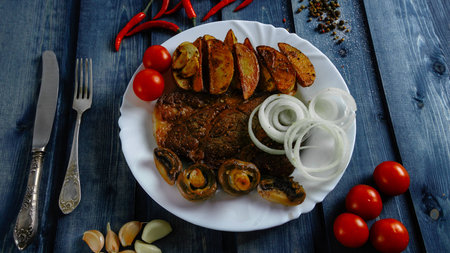 Steak with Idaho potato on a white plate. Blue background. Food on a wooden countertop. Steak with Idaho potatoes on a white plate. Blue background. Eating on a wooden countertop.の写真素材