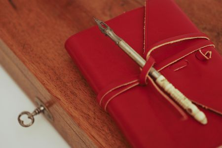 An old wood box with a calligraphy pen on top and  leather red diary  on a white background