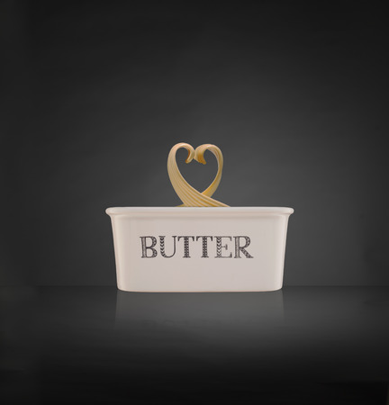 Heart shaped butter curl on top of butter dish with dark background and reflectionの写真素材