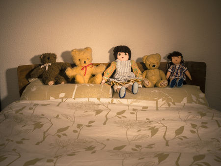 Teddies and Dolls on Bed in bedroom agains headboardの写真素材