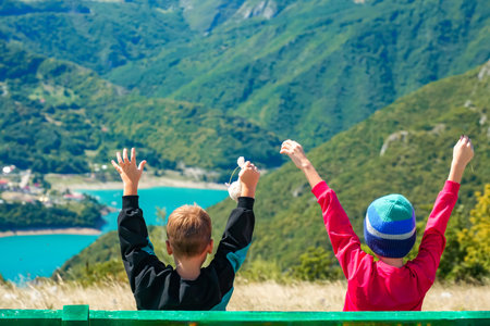 Two boys raising hands on bench with view of Piva Lakeの写真素材