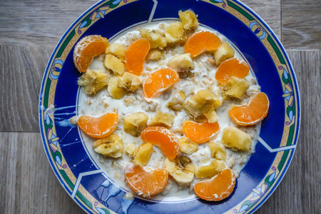 Blue ceramic plate with oatmeal topped with banana and orange slices. Simple homemade breakfast rich...