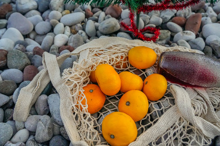 Close-up of mandarins in a net and a red lemonade bottle on a pebbly beach. Festive holiday concept...