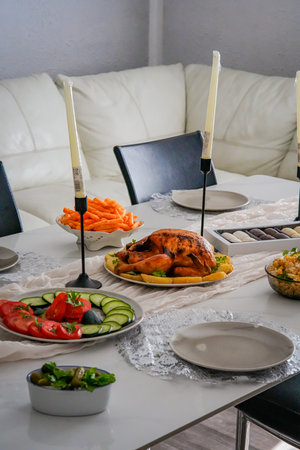 Side view of festive holiday table with candles, roasted chicken, salads, and mandarins