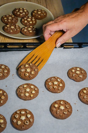Adult hand holding wooden spatula with cookies, plate of cookies nearby