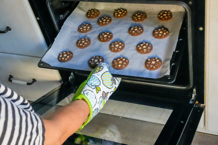 Hand in oven mitt taking baking tray with cookies from oven