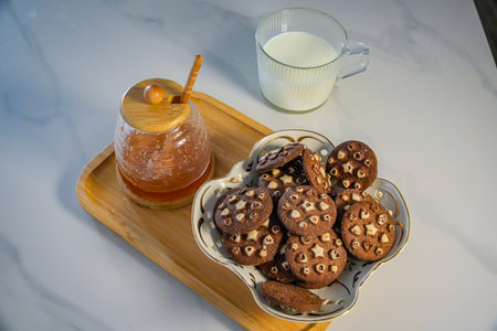 Side angle of cookies tray with honey jar and mug of milk
