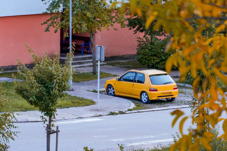Yellow car parked under building entrance with orange autumn leaves in foregroundの写真素材