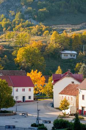 A pair of houses with red roofs against rolling autumn hills with treesの写真素材