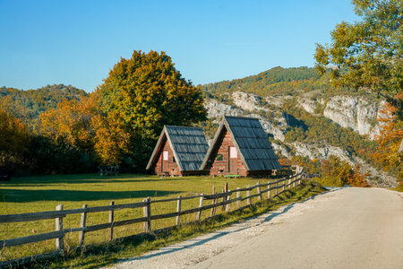 Two triangular wooden houses behind fence under mountainsの写真素材