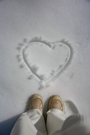 Feet in winter boots standing on snow with heart drawnの写真素材
