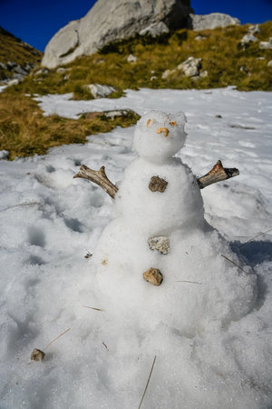 Snowman on snow patch with rocky peaks in background, mid-distance