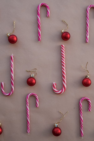 Christmas Pattern of Red and White Candy Canes with Glossy Ornaments on Beige Background