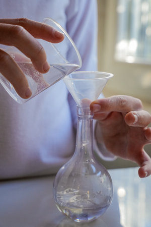 Hands Pouring Liquid into Glass Flask Vertical