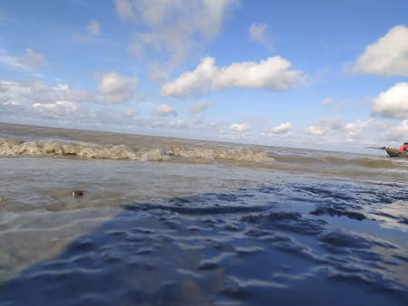 Waves on the beach at low tide. Blue sky with white clouds.の写真素材