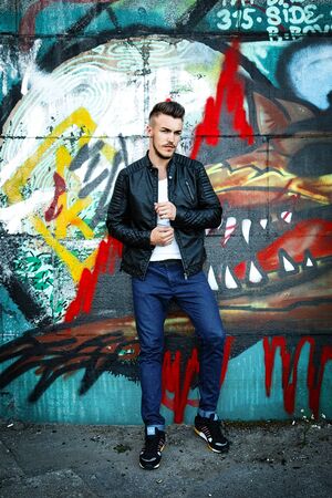 Attractive young man in white shirt and black jacket on graffiti backgroundの写真素材