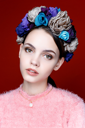 Beautiful model with a wreath of flowers on her head on red background. Beauty Woman face Portrait. Beautiful Spa model Girl with Perfect Fresh Clean Skin.の写真素材