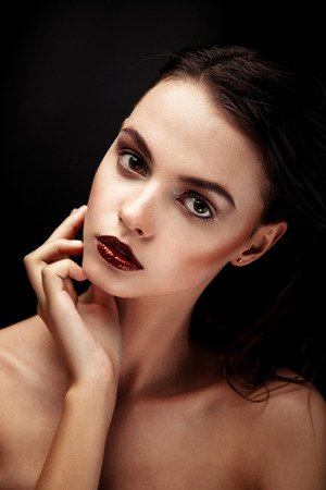 Pretty brunette female model face posing in studio. Beautiful model girl with beauty makeup touching her perfect fresh face skin.の写真素材