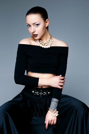 Beautiful female model posing in elegant black clothes in studio. Perfect skin and make up. Beautiful young brunette woman with trendy accessories posing in studio.の写真素材