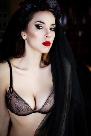 Beautiful woman in stockings and lingerie with a wreath on head. Sexy young woman wearing black lingerie. Perfect skin and make up. Red lipsの写真素材