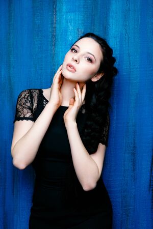 Cute young woman in navy black dress on blue backgroundの写真素材