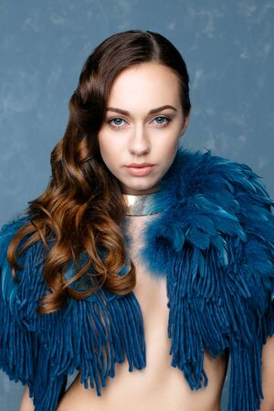 Beautiful young woman in clothes from swan feather posing in studio. Gorgeous lady with blue eyes and brown hair.の写真素材