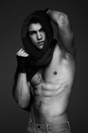 Young fashion topless man in knitted scarf on his had isolated on dark background. black and white photoの写真素材