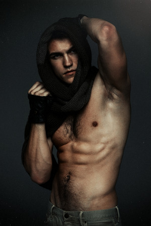 Young fashion topless man in knitted scarf on his had isolated on dark background. Strong Athletic Man Fitness Model Torso showing six pack absの写真素材