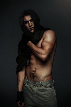 Young fashion topless man in knitted scarf on his had isolated on dark background. Strong Athletic Man Fitness Model Torso showing six pack absの写真素材