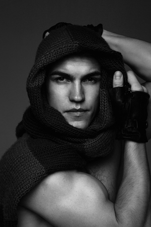 Young fashion topless man in knitted scarf on his had isolated on dark backgroundの写真素材