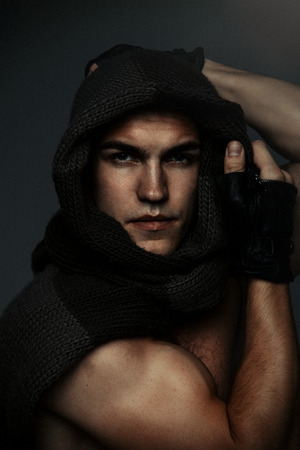 Young fashion topless man in knitted scarf on his had isolated on dark backgroundの写真素材