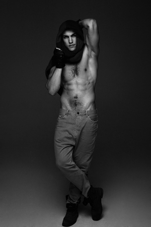Young fashion topless man in knitted scarf on his had isolated on dark background. black and white photoの写真素材