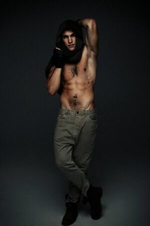 Young fashion topless man in knitted scarf on his had isolated on dark backgroundの写真素材